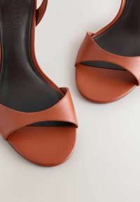 Paire de sandales en cuir marron à bout ouvert avec une seule sangle large et des semelles intérieures noires sur un fond clair.
