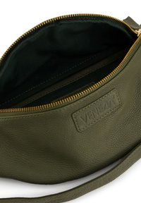 Olivgrüne Ledertasche mit einer strukturierten Oberfläche, goldfarbenem Reißverschluss und einem dunkelgrünen Stofffutter. Verfügt über ein Logo-Patch im Inneren.