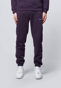 Purple sweatpants made of soft fabric, featuring a slim fit, elastic cuffs, and subtle stitching details, paired with white sneakers.
