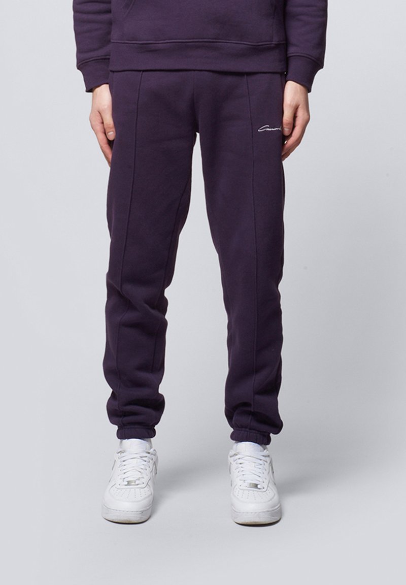 Purple sweatpants made of soft fabric, featuring a slim fit, elastic cuffs, and subtle stitching details, paired with white sneakers.
