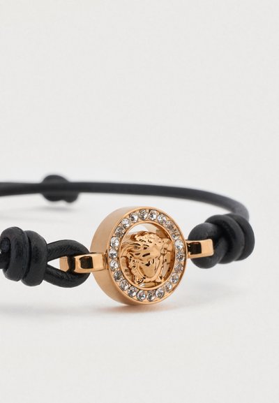 Juodos odos apyrankė su apvalia aukso spalvos sagtimi, kurioje pavaizduotas liūto simbolis, apsuptas skaidrių cirkonio akmenėlių apskritimu.