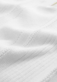 Biały materiał o wzorze dzianiny z fakturą, z delikatnymi prążkami i miękkim, gładkim wykończeniem. Światło odbija się od jego powierzchni.