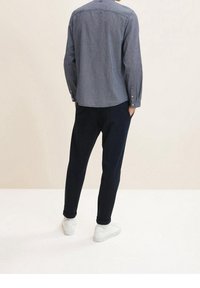 Camicia a maniche lunghe a righe navy, dalla vestibilità rilassata, abbinata a pantaloni scuri e sneakers bianche. Tessuto morbido, motivo sottile sulla stoffa.