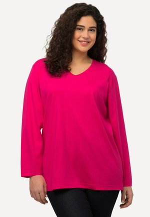 Top lungo fucsia con scollatura a V, realizzato in un tessuto morbido. Presenta una vestibilità rilassata e delle leggere fessure laterali per il massimo comfort.