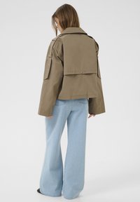 Khaki jas met een kraagontwerp, zijzakken en drukknoopdetails; gecombineerd met lichtblauwe flared jeans; zachte stoftextuur.