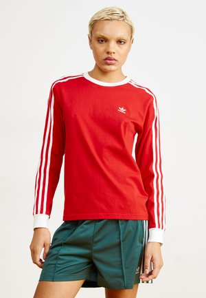 Red long-sleeve shirt made of cotton with white accents, featuring a crew neckline and three white stripes along the sleeves. Pair of dark green shorts.