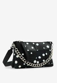 Borsa a tracolla a pois bianca e nera con una texture intrecciata, dotata di una tracolla in metallo e spallacci regolabili.