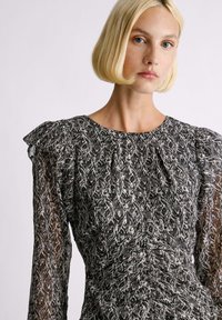 Vestido a rayas en blanco y negro con largas mangas de tul, acentos de hombros con volantes y un diseño ajustado en la parte superior y acampanado en la parte inferior. Tejido texturizado.