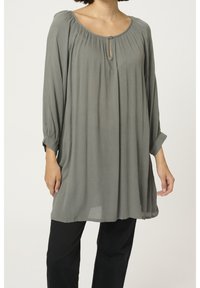 Túnica de manga larga en tejido verde apagado, con un escote redondeado, detalles de plisados y un pequeño botón en la parte frontal.