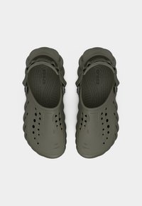 Ζευγάρι από χακί Crocs με οπές αερισμού, ρυθμιζόμενα λουριά στη φτέρνα και υφασμένα πέλματα, εμφανιζόμενα από πάνω σε λευκό φόντο.
