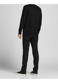 Černá mikina s dlouhými rukávy a kulatým výstřihem, spárována s černými slim-fit kalhotami a černými teniskami s bílou podešví.