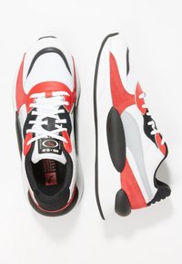 Running shoes with a mesh upper in white, red, and black. Features include a padded tongue, flat laces, and a textured sole.