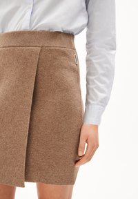 Gonna di maglia marrone con vita a costine e design avvolgente. Il tessuto sembra morbido e strutturato, abbinato a una camicia colletto blu chiaro.