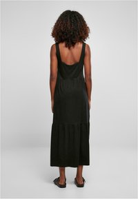 Černé maxi šaty bez rukávů s vykrojeným zádům, s nařaseným pasem a vrstveným lemem. Vyrobené z měkkého materiálu s hladkou texturou.