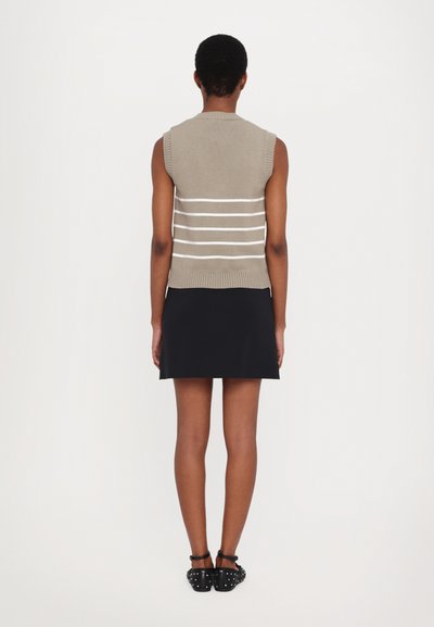 Kätsega kampsun beež, millel on valged horisontaalsed triibud, koos musta seeliku ja nähtavate jalgadega, jalas mustad neliudele mütsiga kingad.