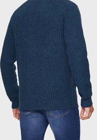 Donkerblauwe gebreide trui met een gestructureerd patroon, geribbelde manchetten en een iets losse pasvorm, gedragen met een blauwe spijkerbroek.