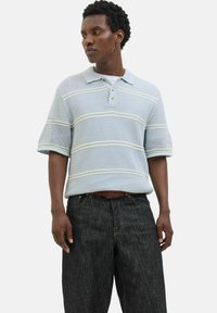 Lyseblå strikket polo med korte ærmer, prydet med stribede mønstre og en tre-knaps lukning, parret med mørk denim jeans.