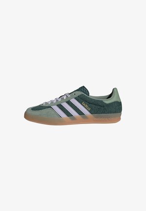 Baskets vertes Adidas Gazelle avec des bandes blanches, texte doré « "GAZELLE" », lacets blancs, texture en suède et semelle en gomme, vue de côté.