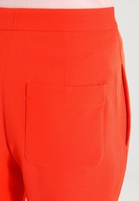 Feloranje broek van een textuurstof, met een enkele zak op de achterkant en een gladde tailleband.
