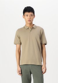 Khaki koszulka polo wykonana z bawełny, z klasycznym kołnierzykiem, krótkimi rękawami i subtelnym logotypem na piersi. Noszona z zielonymi spodniami.
