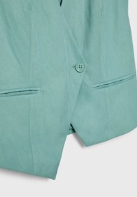 Veste bleu sarcelle clair avec un seul bouton rond et deux poches horizontales fendues à l'avant.