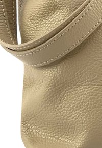 Beige lederen tas met een textuur, heeft een lange schouderriem; stiksels zichtbaar langs de randen van de riem.