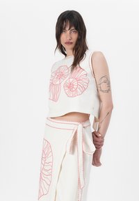 Set in lino composto da un top corto e una gonna di colore crema con ricami a spirale rossi. Il top presenta un collo rotondo e uno stile senza maniche con una vita annodata.