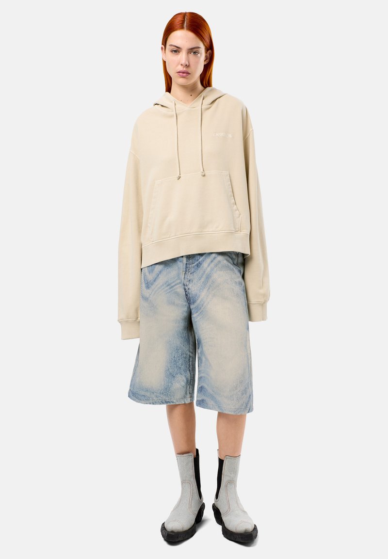 Hoodie cropped beige avec poche avant, associé à un short en denim bleu clair avec un motif de décoloration. Des bottes chelsea grises complètent le look.