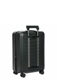 Valigia rigida nera con superficie testurizzata, manico retrattile e quattro ruote per la mobilità. Chiusura con zip lungo un lato.