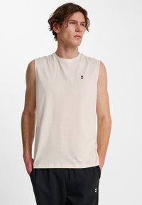 Krämfärgad ärml�ös t-shirt i mjukt material, med rund halsringning och tre svarta chevroner på vänster bröst.