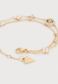 Βραχιόλι σε χρυσή απόχρωση που διαθέτει πολλαπλές αλυσίδες, στολισμένο με στρογγυλά και αστεροειδή μενταγιόν, διαυγείς στρας και μια τριγωνική ετικέτα.