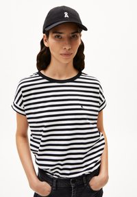 Schwarz-weißer gestreifter T-Shirt mit aufgerollten Ärmeln und rundem Halsausschnitt, kombiniert mit einer schwarzen Kappe mit weißem Logo. Lässiger Schnitt.