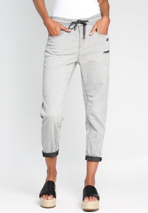 Pantalon jogger gris clair avec poignets, cordon noir et poche latérale, porté avec des sandales plateformes noires sur une personne debout.