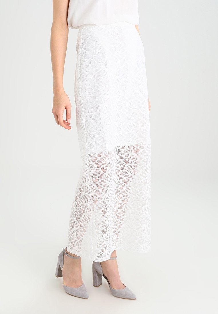 Gonna maxi bianca in pizzo con motivo floreale, tessuto semi-trasparente, foderata sotto, abbinata a scarpe con tacco alto grigie.