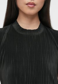 Fekete redőzött felső, texturált felülettel, kerek nyakkivágással és ujjatlan ujjakkal, finom függőleges redőzésekkel az egész felületen.