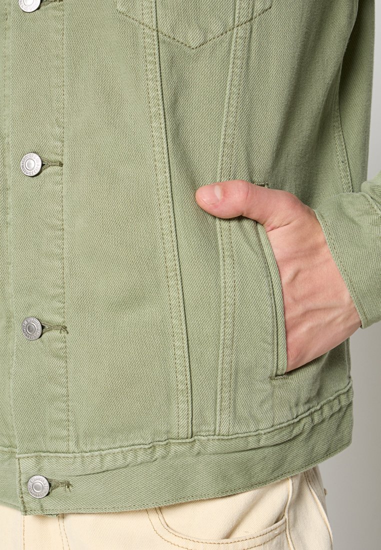 Giacca in denim verde con bottoni argentati, una tasca sul petto, tasche sui lati e dettagli di cucitura visibili. Tessuto morbido e strutturato.