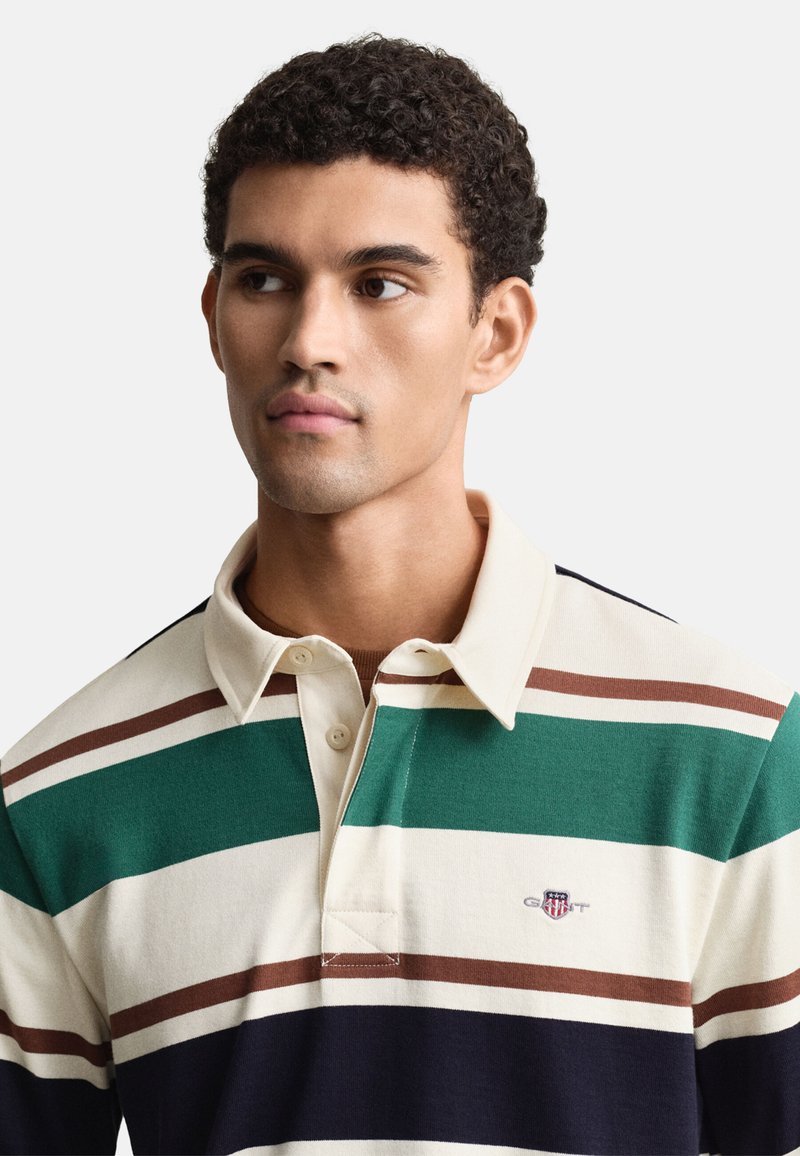 Striped cotton polo shirt with a beige base, featuring green, brown, and navy stripes. Includes a collar and front buttons. GANT logo displayed.