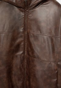 Tmavě hnědá kožená bunda s viditelnými ševmi a středovým předním zipem.