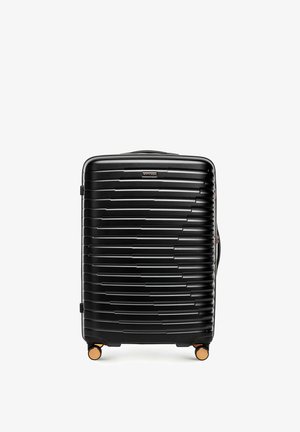 Černý kufr s pevnou skořepinou, horizontálními rýhami, čtyřmi zlatými otočnými kolečky a horním madlem, zobrazený zepředu na bílém pozadí.