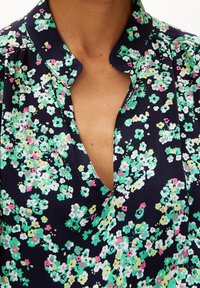 Blouse florale avec un fond bleu marine foncé et un motif délicat de fleurs vertes et roses, dotée d'un col et d'un décolleté en V profond.