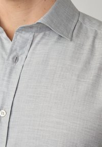 Lichtgrijs overhemd met knoopsluiting en een visgraatstructuur, voorzien van een puntige kraag en een enkele knoopsluiting bij de hals.