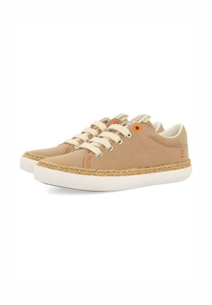 Zapatillas de lona beige con suelas de goma blanca, acentos de yute, ojales de metal, cordones beige y un detalle naranja cerca del ojal.