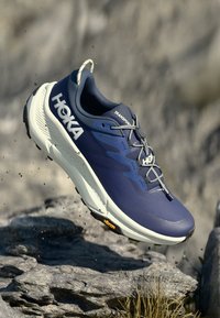Chaussure de randonnée bleu marine avec une tige en mesh texturé, semelle rembourrée et lacets réfléchissants. Equipée d'une semelle extérieure Vibram pour une meilleure traction.