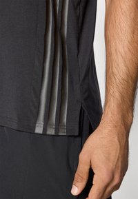 Μαύρο αθλητικό πουκάμισο με ανοιχτό γκρι πλέγμα στα πάνελ και πλαϊνές σχισμές. Διαθέτει κοντά μανίκια, στρογγυλεμένη άκρη και απαλό ύφασμα από βαμβακερό μείγμα.