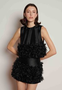 Μαύρο φόρεμα με κομψό σατέν τοπ και στρωμένο υφασμάτινο βολάν στη μέση και το τελείωμα. Δομημένο, κοντό σχέδιο με λεπτομέρειες άνθινης υφής.