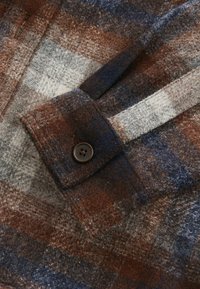Braun-, Marineblau- und Graustreifen-Flanellhemd-Detail mit einem geknöpften Manschette und strukturiertem Stoff mit einem leicht fuzzy Aussehen.