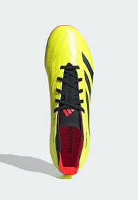 Scarpa da calcio gialla brillante con superficie testurizzata, lacci neri e tre strisce nere. Presenta un interno rosso e un branding prominente.