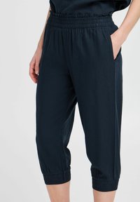 Pantalons cropped bleu marine en tissu léger. Dotés d'une taille élastique avec des détails en volants et de poignets élastiques. Comprend des poches latérales.