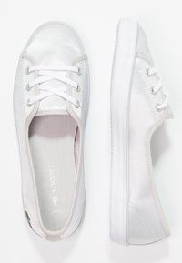 Baskets blanches en toile à texture lisse, bout arrondi, lacets blancs et marquage discret sur la semelle intérieure. Semelle en caoutchouc avec une légère adhérence.