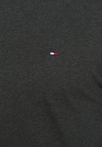 Ciemnoszara tkanina z małym, haftowanym prostokątnym logo w białych, granatowych i czerwonych nitkach, umieszczonym na środku materiału.